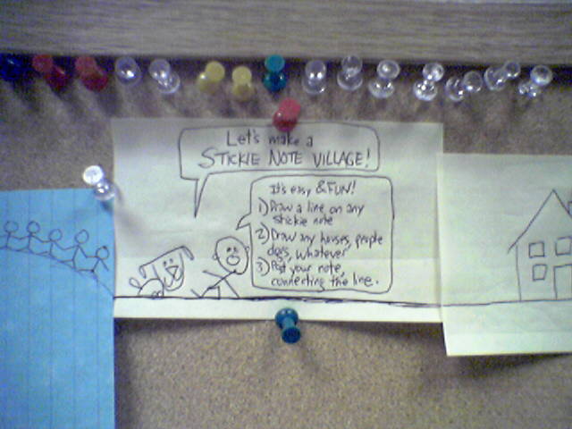 Sticky note on a bulletin board. On the sticky note is a drawing of a dog and a person. The dog is saying, "Let's make a STICKIE NOTE VILLAGE!". The person is saying, "It's easy & FUN! 1) Draw a line on any sticky note. 2) Draw any houses, people, dogs, whatever. 3) post your note, connecting the line.