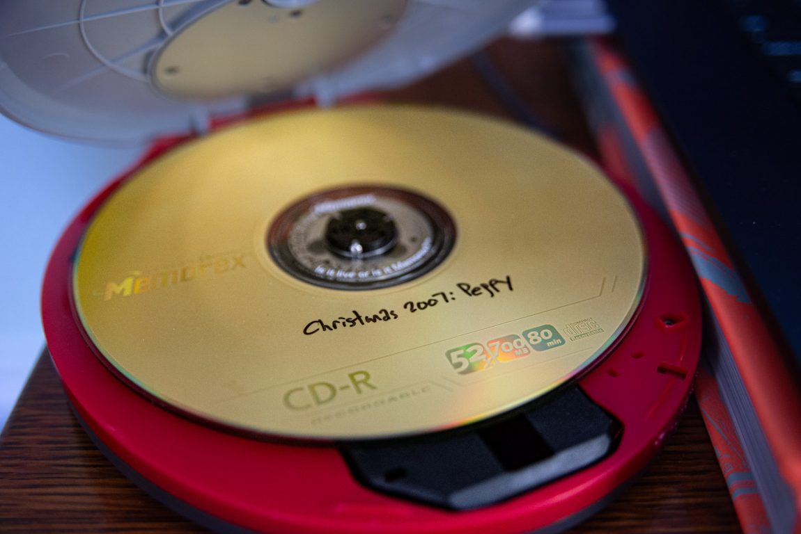Photo of a CD-R mix CD in a portable CD player. The CD is a gold disc with the Memorex logo. Hand-written on the CD in Sharpie is "Christmas 2007: Peppy".