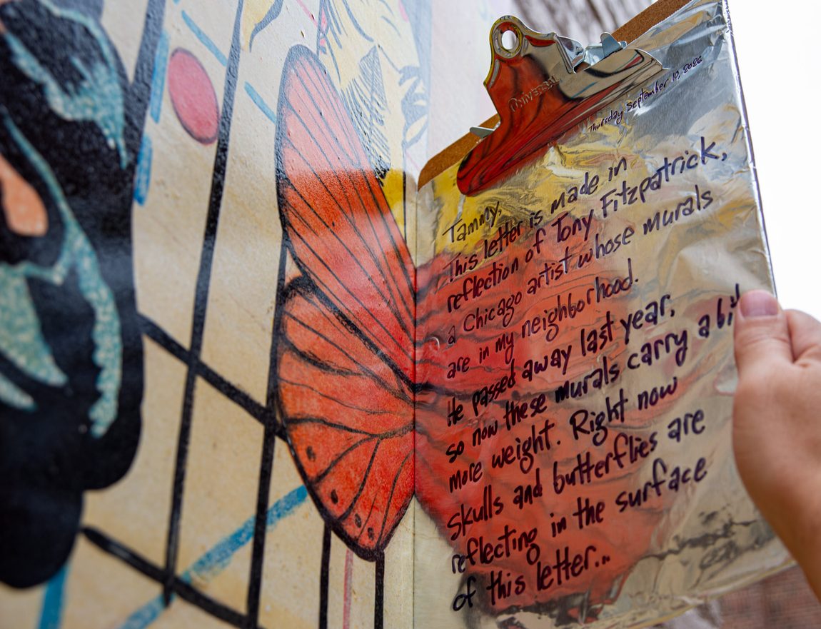 Clipboard wrapped in aluminum foil is positioned next to the Tony Fitzpatrick mural in Glen Ellyn, Illinois. The foil reflects the butterfly in the mural. On the aluminum foil is a letter that says, "This letter is made in reflection of Tony Fitzpatrick, a Chicago artist whose murals are in my neighborhood. He passed away last year, so now these murals carry a bit more weight. Right now skulls and butterflies are reflecting in the surface of this letter..."