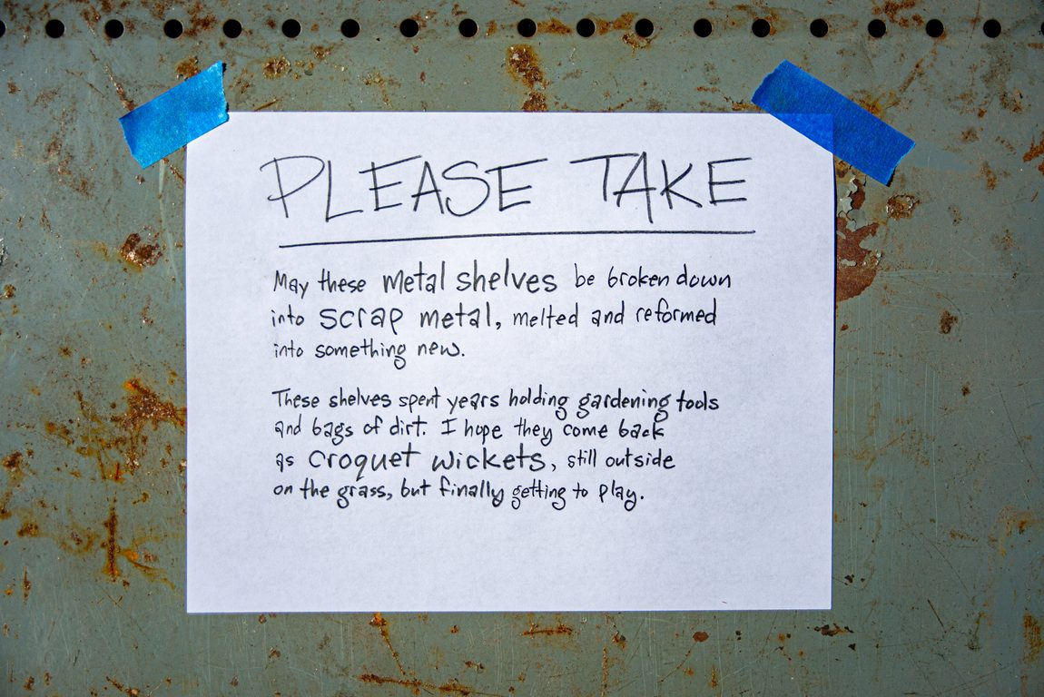 Close up of metal shelf with handwritten letter-sized sign written with a Blackwing pencil (volume 4, Mars and the Perseverance Rover mission). Message is taped on with painter's tape. 